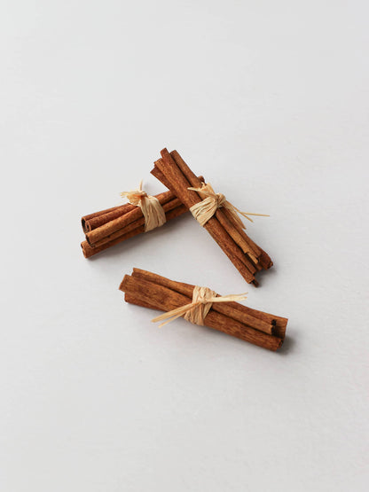 Three bundles of cinnamon sticks tied with raffia for Christmas wreath making, on a neutral background.