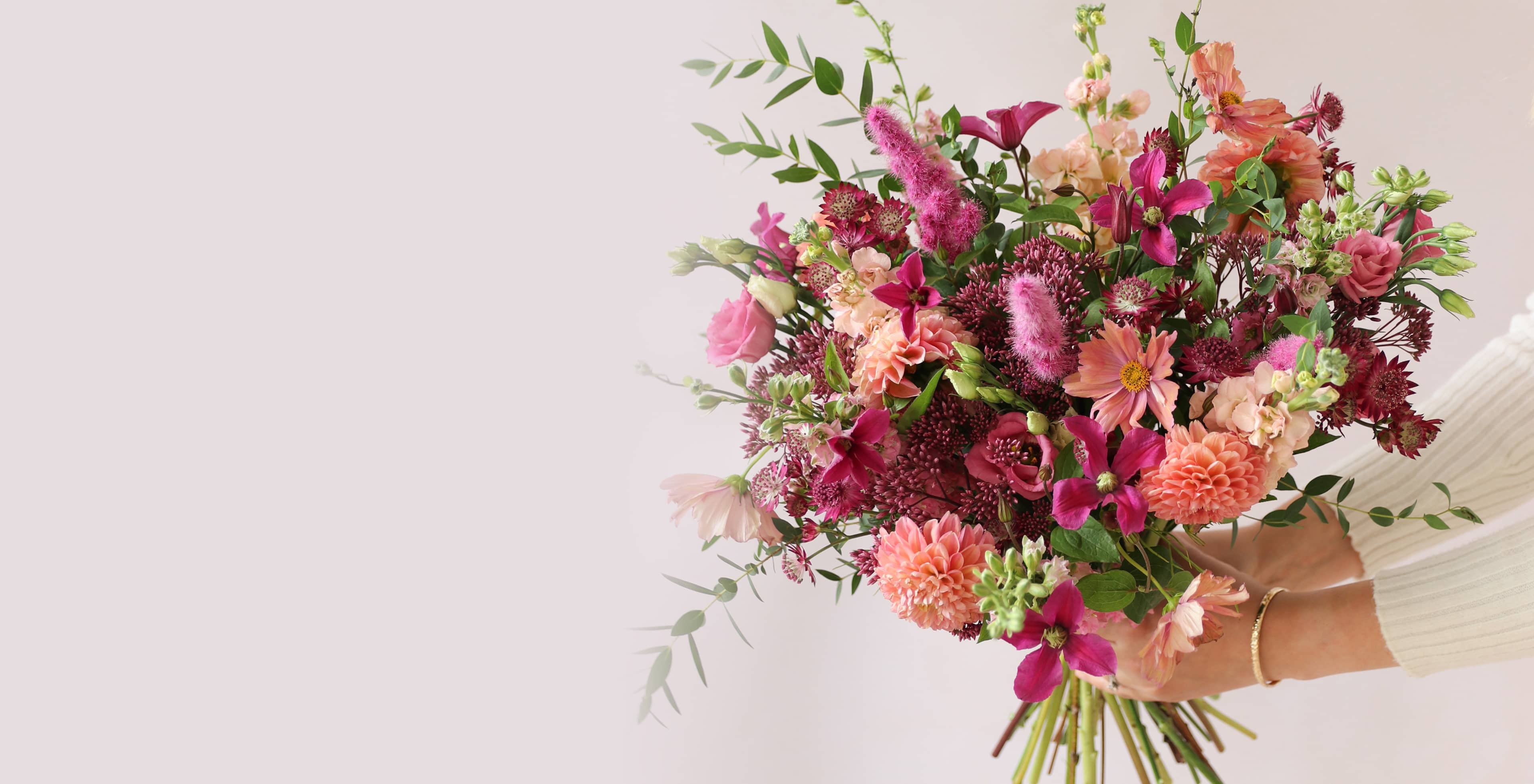 A bouquet of colourful flowers held out to the side by a person against a white background.