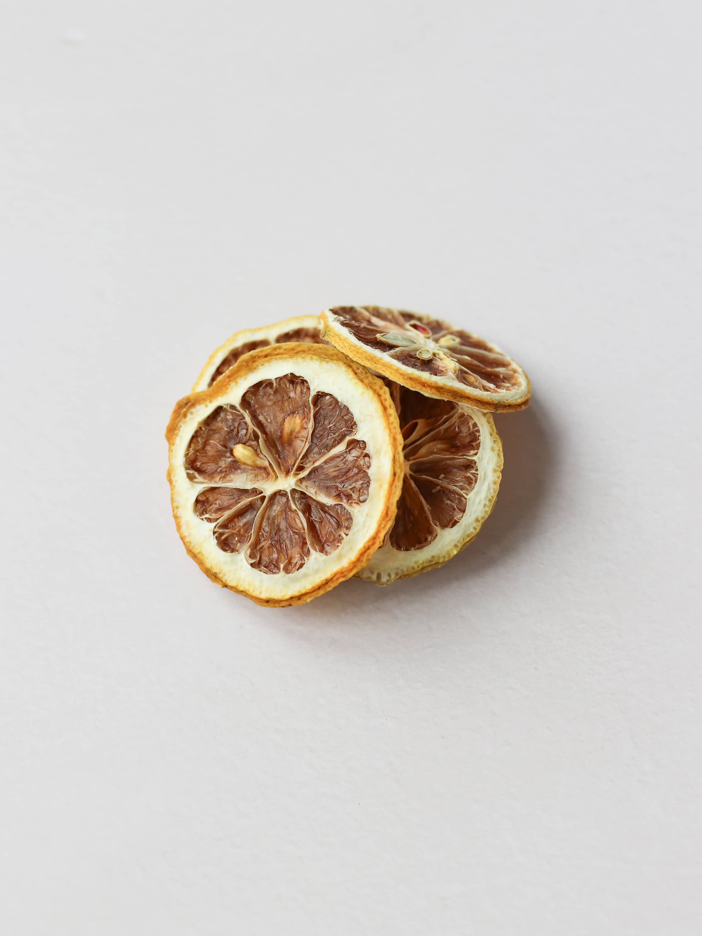 A top view of 5 dried lemon slices stacked on a light neutral background.
