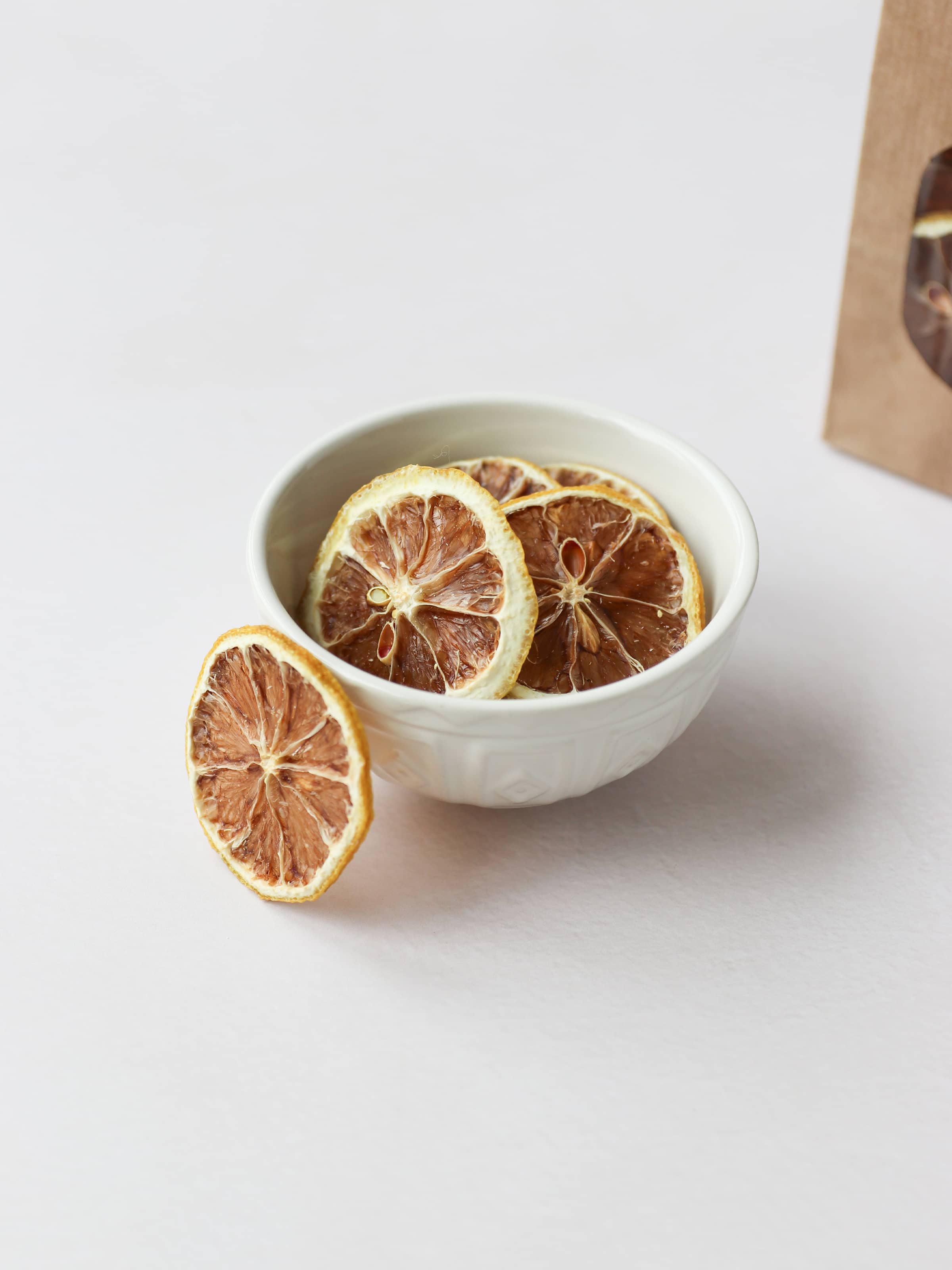 5 dried lemon slices positioned in a decorative cream bowl on a light neutral background.