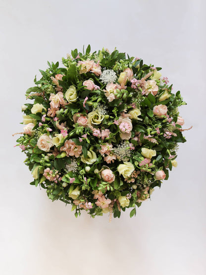 Round funeral posy with white and pastel flowers on a white background