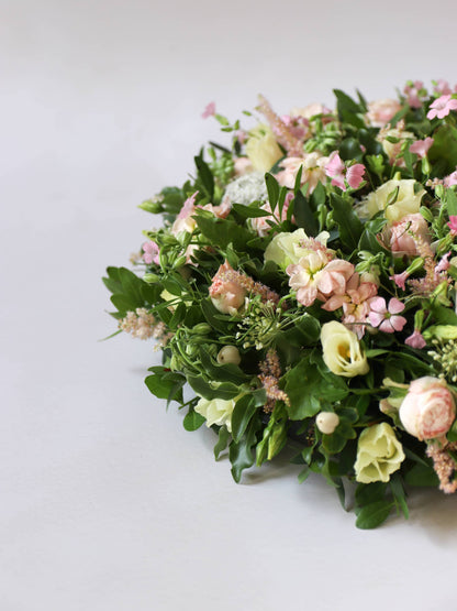 Close up of a round funeral posy with white and pastel flowers on a white background
