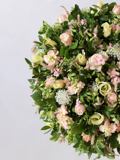 Close up of a round funeral posy with white and pastel flowers on a white background