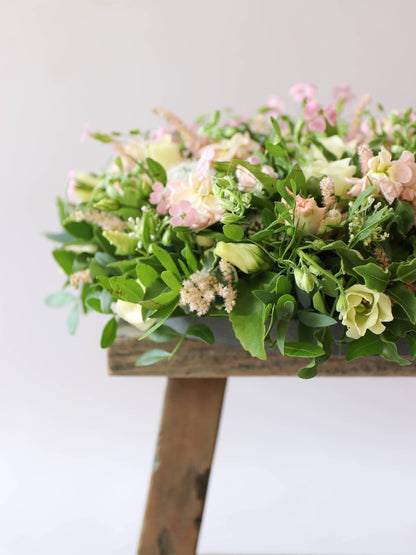 Side view of a round funeral posy with white and pastel flowers on a white background sitting on a wooden stool