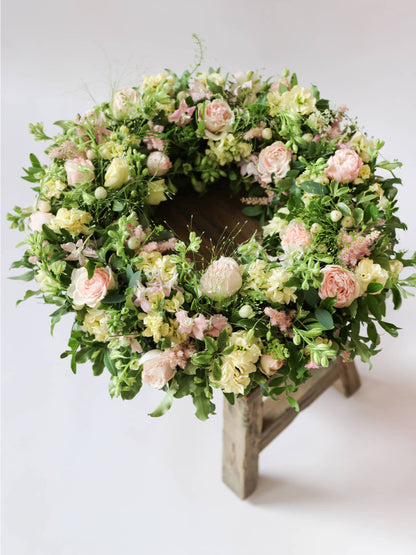 Funeral wreath with pastel and green flowers on a wooden stool against a white background