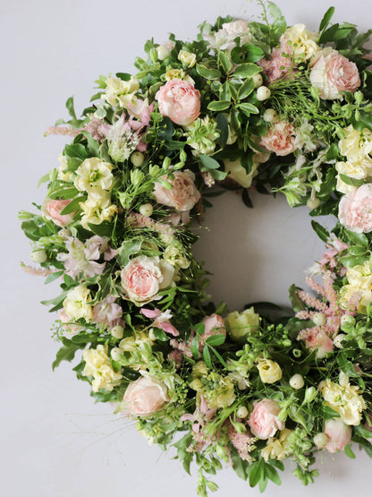 Top down view of close up image of a funeral wreath with pastel and green flowers against white background
