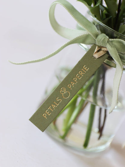 A close up of a green and gold foiled Petals & Paperie brand tag on a bouquet of flowers