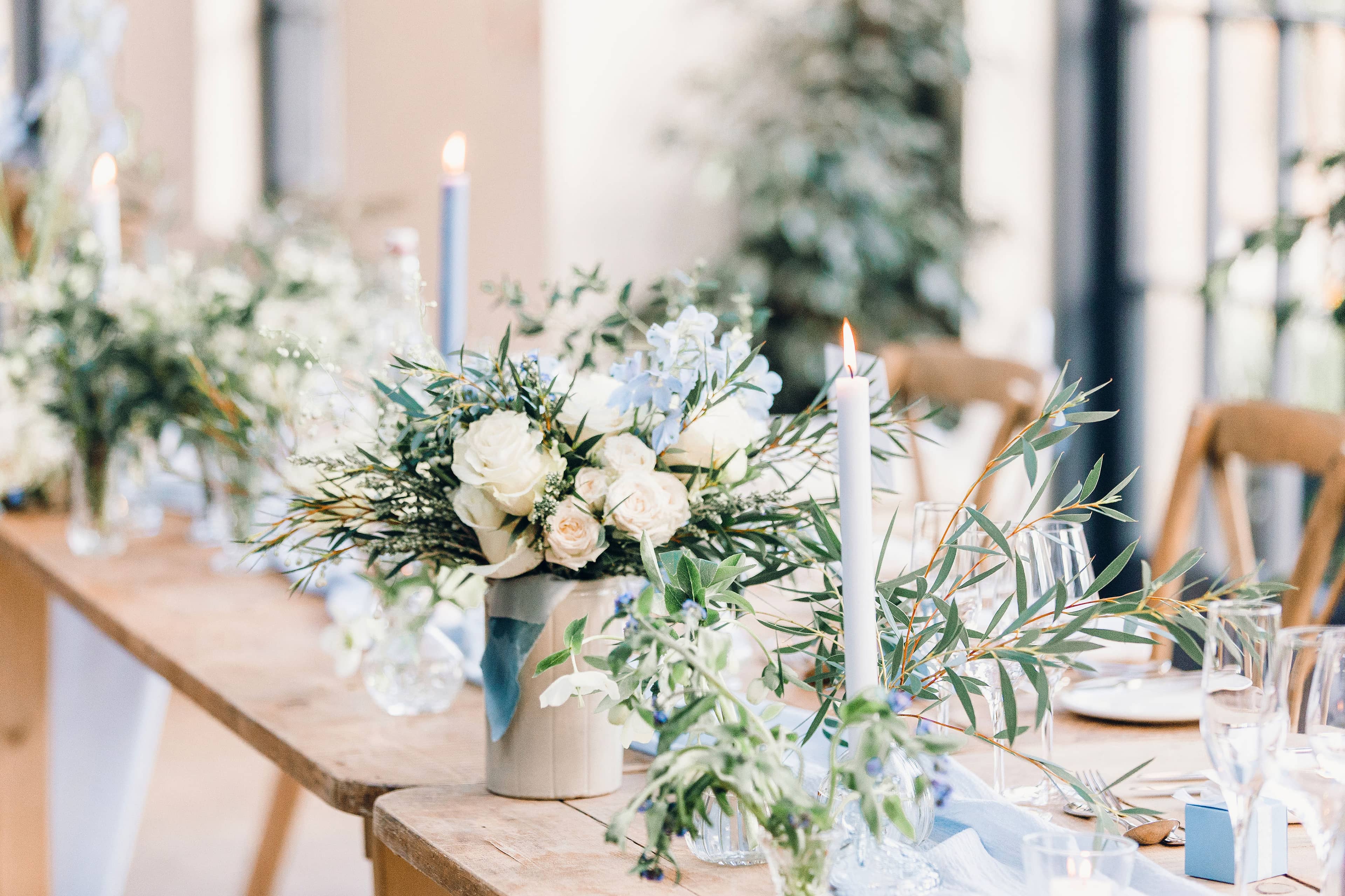 Decorative wedding table setting with white and blue floral arrangements and blue dinner candles in a softly lit room at The Fig House, Middleton Lodge.