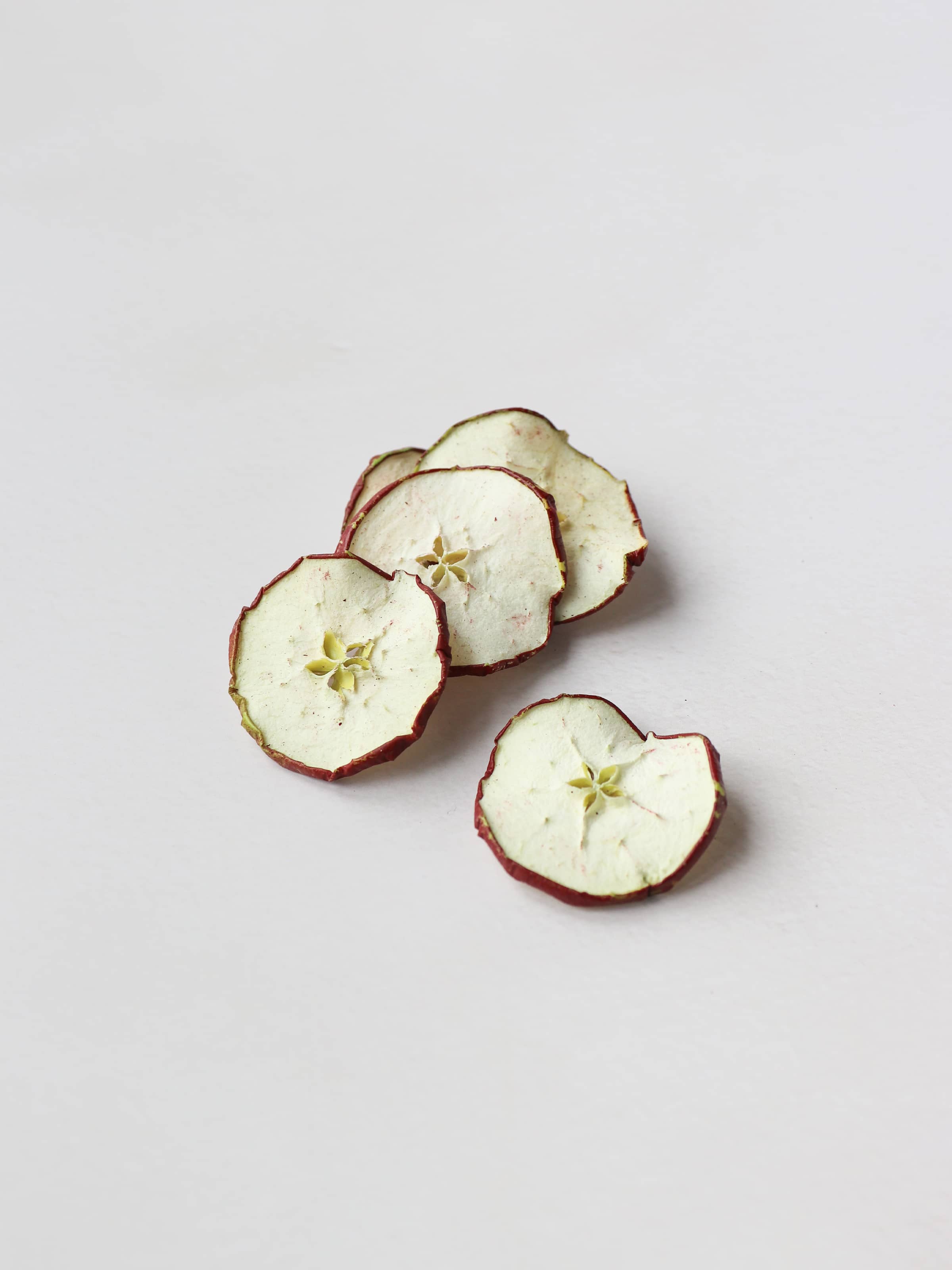 A stack of 5 dried red apple slices for Christmas wreath making lying on a light background.