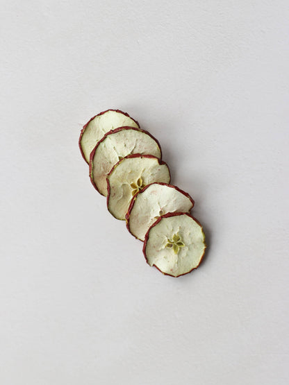 5 sliced dried red apples arranged in a row on a light background.