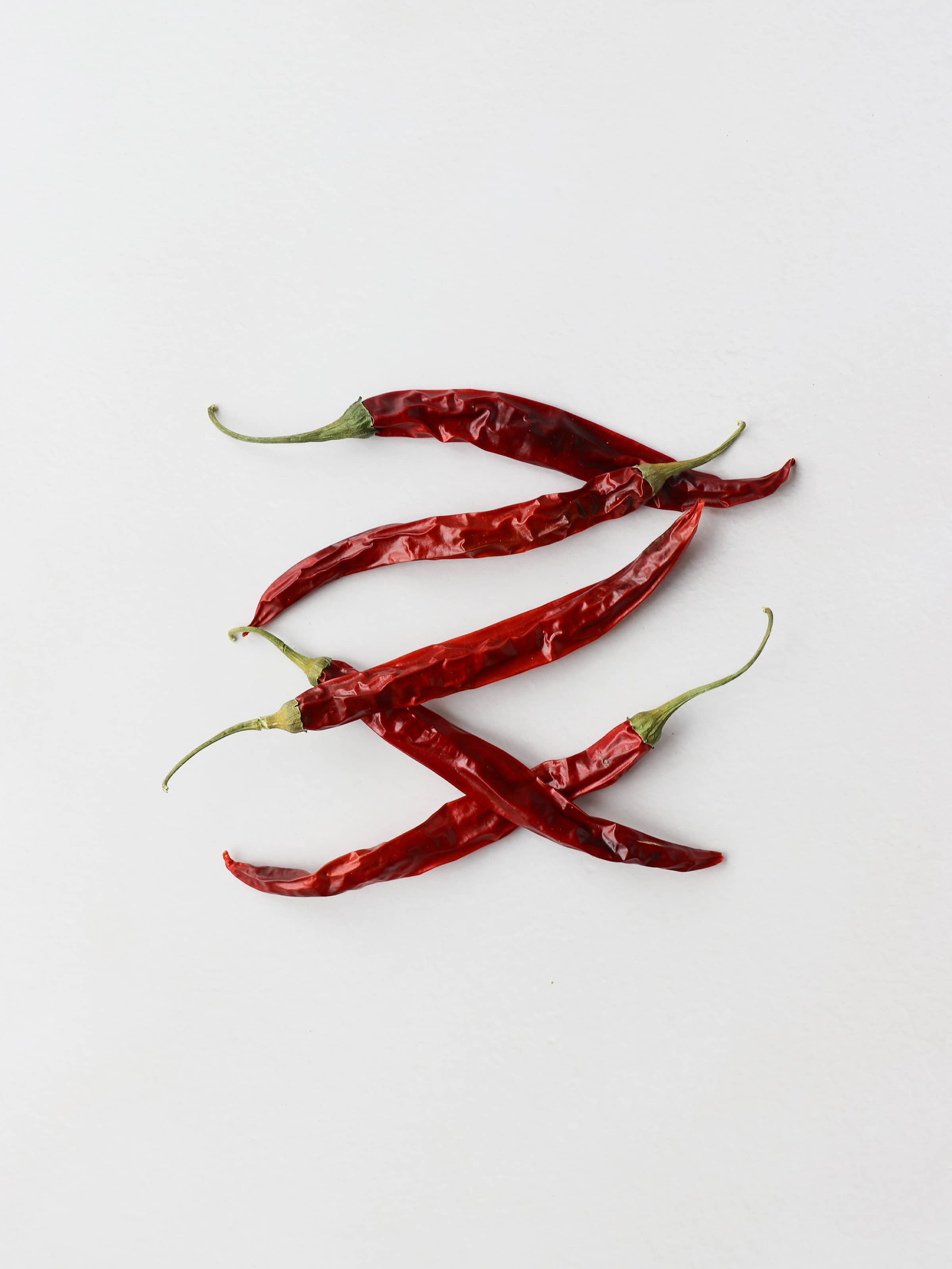 5 dried red chillies for Christmas wreath making, lying on a light background.