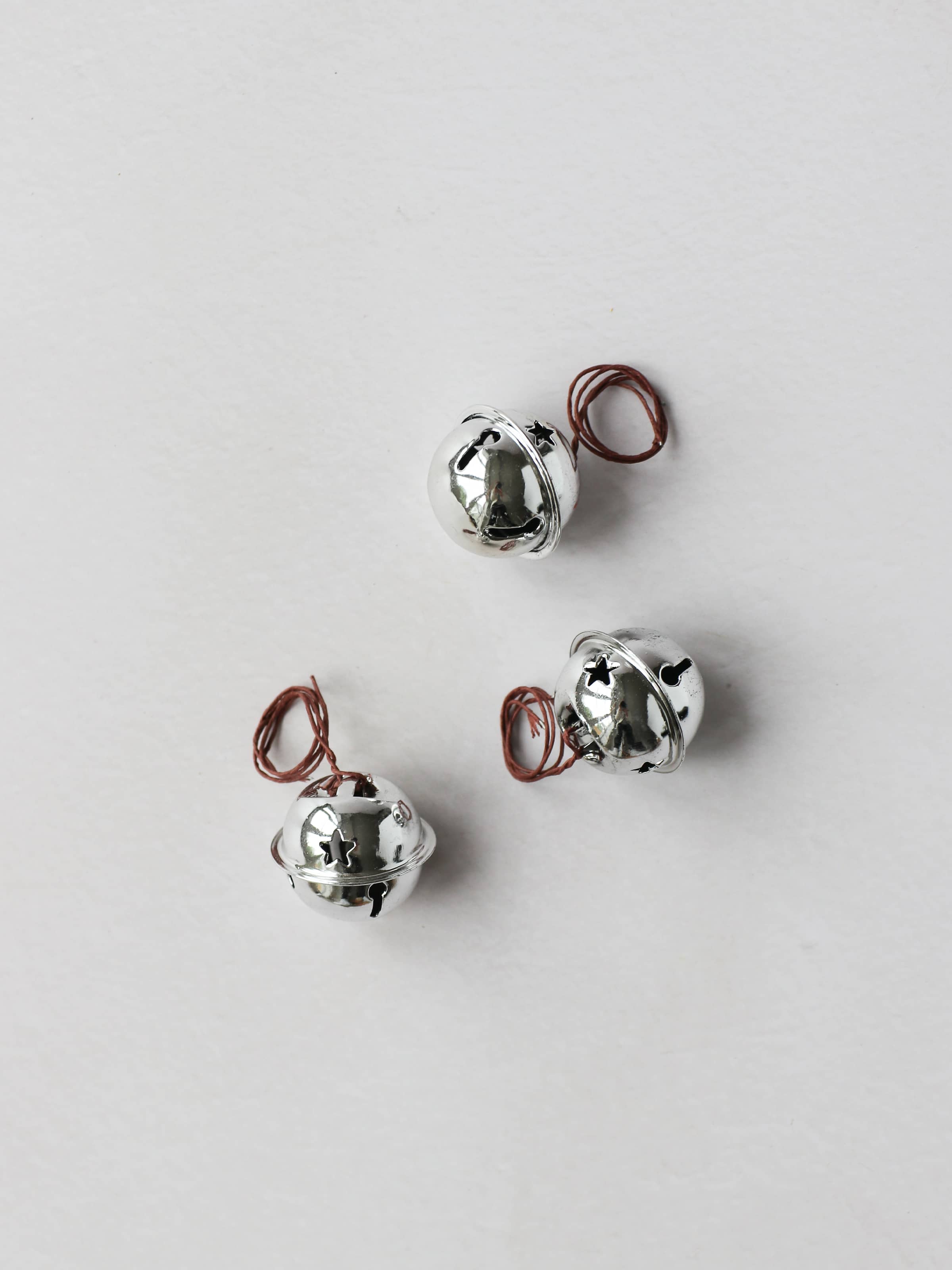 3 silver jingle bells, sitting on a light grey background
