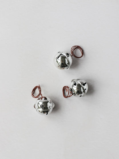 3 silver jingle bells, sitting on a light grey background