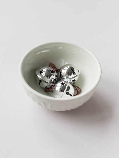 A small cream bowl with 3 silver jingle bells, sitting on a light grey background