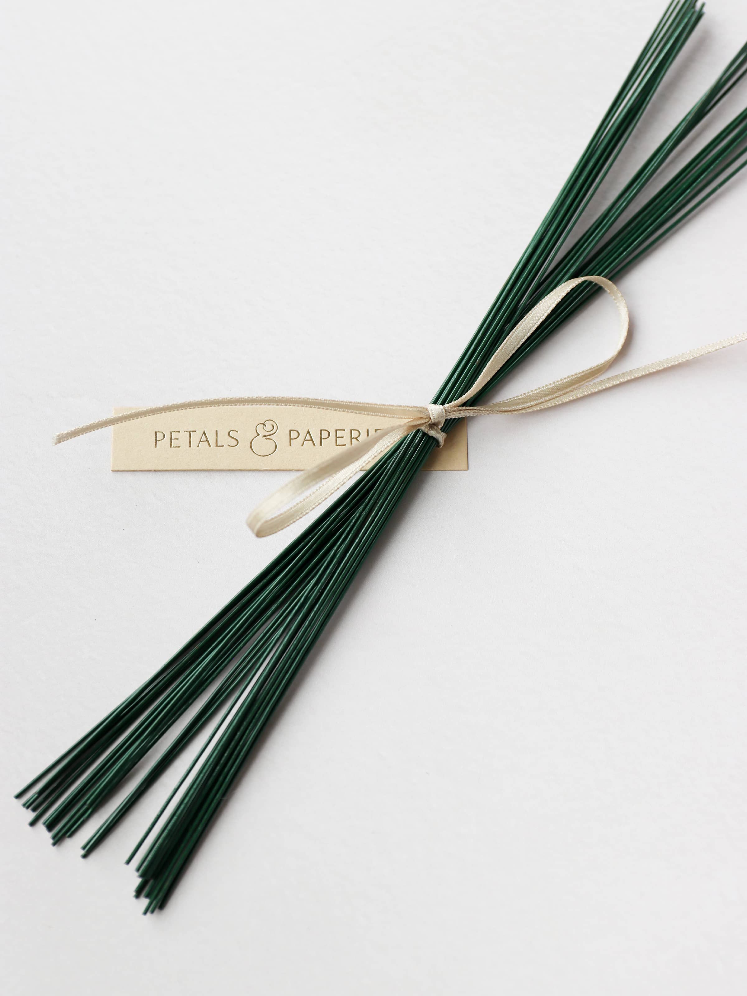 A close up image of a selection of green stub wires tied together with a satin ribbon and a Petals & Paperie gift tag.