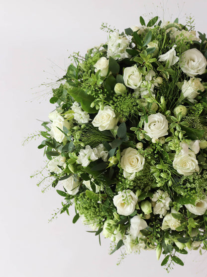 Close up of a round funeral posy with white and green flowers on a white background