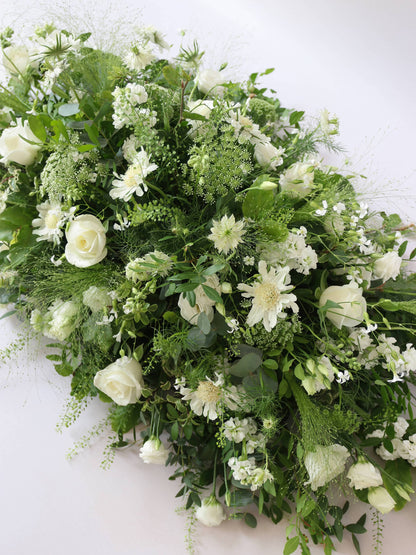 A top view of a 3ft coffin spray featuring white and green flowers and foliage. The funeral arrangement is sitting against a neutral background and features white Roses, Ammi, Stocks and Lisianthus. 