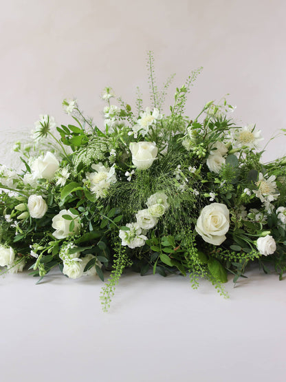 A close up of the middle section of a 3ft coffin spray featuring white and green flowers and foliage. The funeral arrangement is sitting against a neutral background and features white Roses, Ammi, Stocks and Lisianthus. 