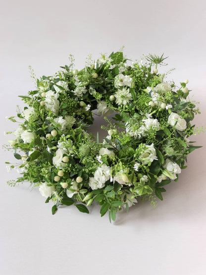 Funeral wreath with white and green flowers against a white background