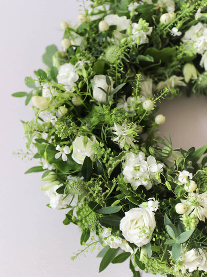 Close up of a funeral wreath with white and green flowers against a white background
