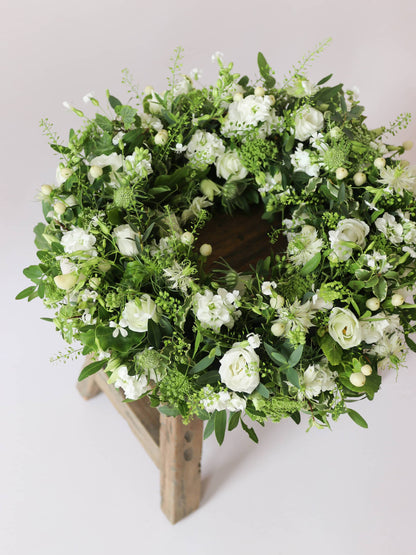 Funeral wreath with white and green flowers on a wooden stool against a white background