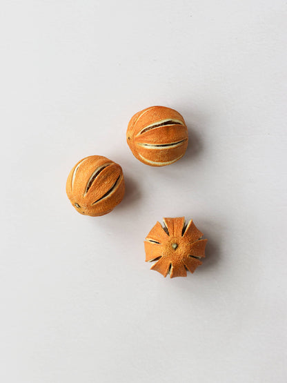 A top down view of three dried whole oranges for Christmas wreath making, positioned on a light background.