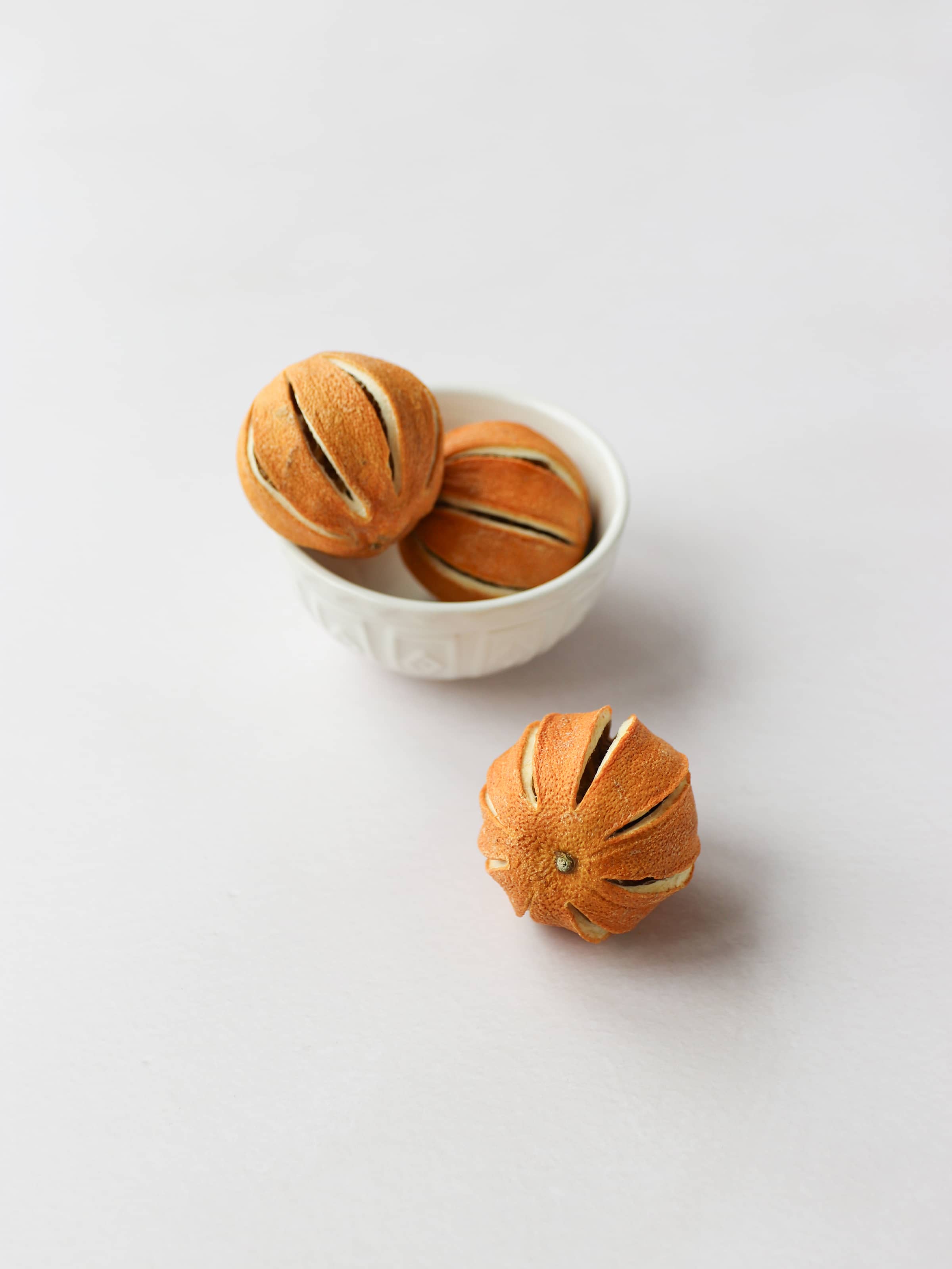 Three dried whole oranges for Christmas wreath making, positioned in a cream decorative bowl, on a light background.
