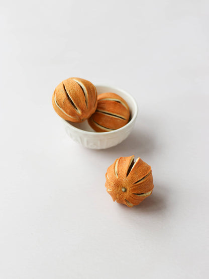 Three dried whole oranges for Christmas wreath making, positioned in a cream decorative bowl, on a light background.